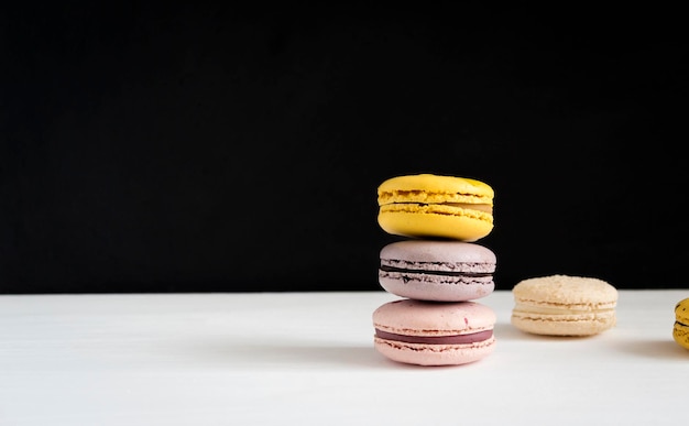 A stack of bright macaroons on a white black background dessert\
of yellow purple and pink color closeup on the table banner\
template with copy space