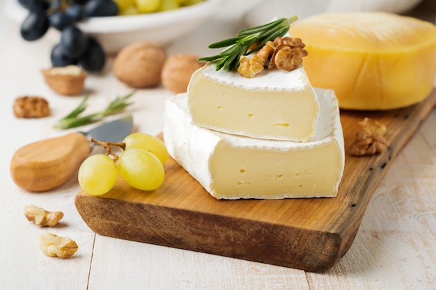 Impilare il formaggio camembert con uva, noci e basilico su una superficie di cemento grigio chiaro