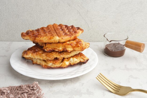 Stack of Caramelized Croissant Waffle or Croffle served in white plate on grey background Close up