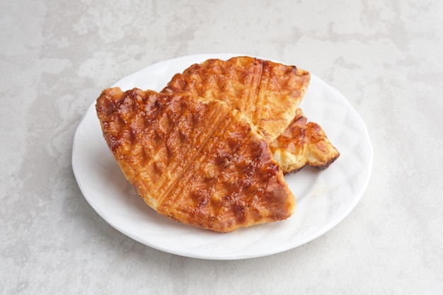 Stack of Caramelized Croissant Waffle or Croffle served in white plate on grey background Close up