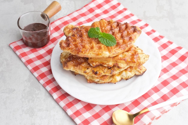 Pila di cialde di croissant caramellate o croffle servite in un piatto bianco su sfondo grigio primo piano