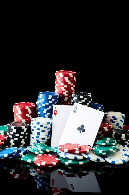 Stack of casino gambling chips and cards isolated on black\
reflective background