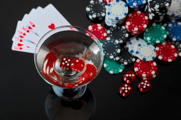 Stack of casino gambling chips glass of martini vermouth and red dices isolated on reflective black ...