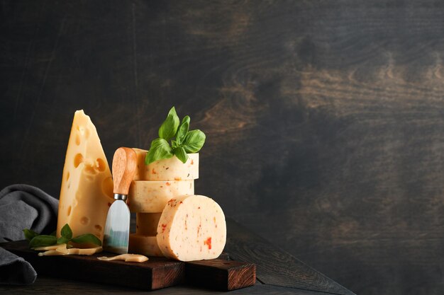 Stack of cheese with tomatoes and seasoning and swiss cheese on\
with basil and knife on serving board on dark wooden table\
background assortment of different cheese types cheese\
background