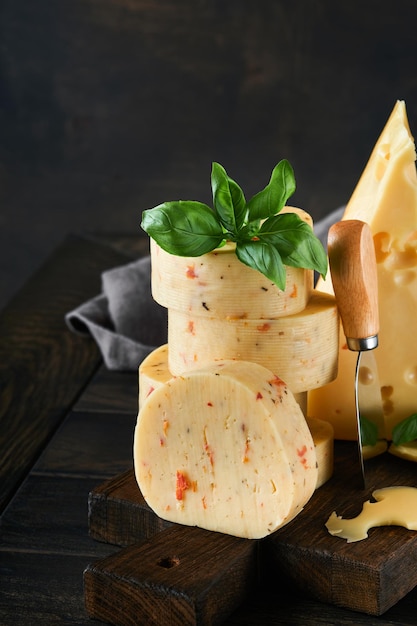 Stack of cheese with tomatoes and seasoning and swiss cheese on\
with basil and knife on serving board on dark wooden table\
background assortment of different cheese types cheese\
background