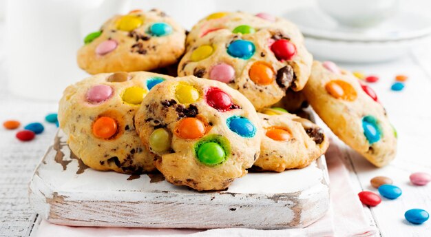 Stack of children's cookies with colorful chocolate candies in a sugar glaze on a white light wooden background. Selective focus.