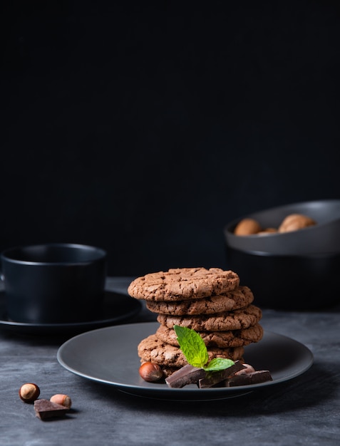 A stack of chocolate chip cookies with chocolate chips, nuts and mint  on a dark table. Front view and copy space