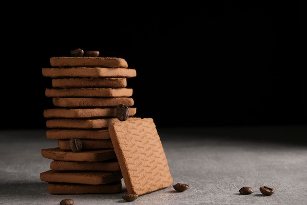 Stack of chocolate cookies and scattered coffee beans on black background