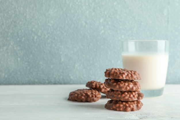 Stack of chocolate cookies with glass of milk on white table against light background