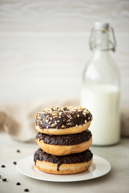 a stack of chocolate glazed donuts with coffee and milk on a white table