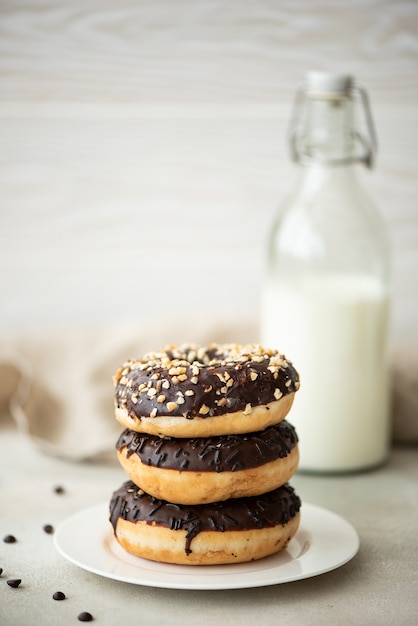 A stack of chocolate glazed donuts with coffee and milk on a white table