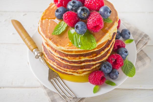 Stack of classic  American pancakes with fresh berries and maple syrup, on white table background copy space