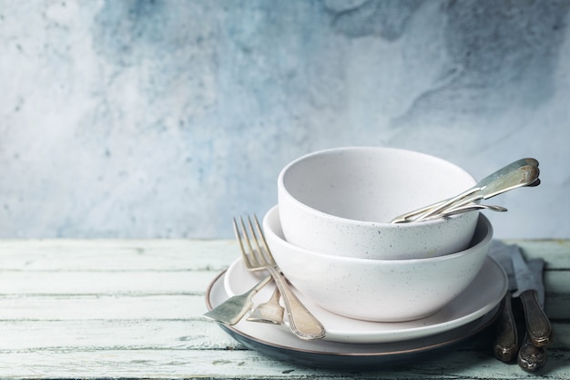 Stack of clean dinner plates with cutlery on top over wooden table. Pastel tones.