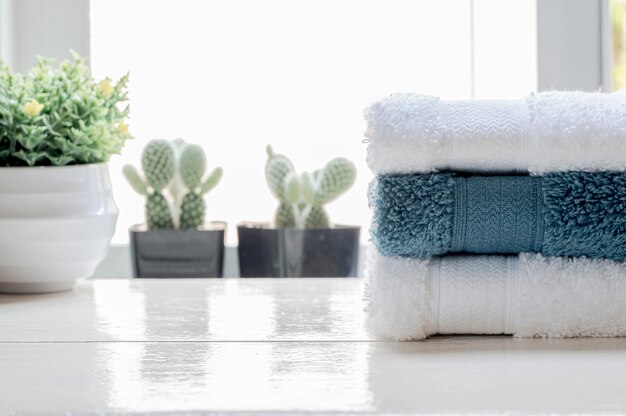 Stack of clean towels and houseplant on white wooden table