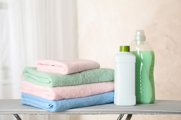 Stack of clean towels and laundry liquid on ironing board, 