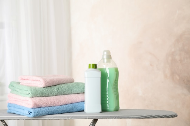 Stack of clean towels and laundry liquid on ironing board, 