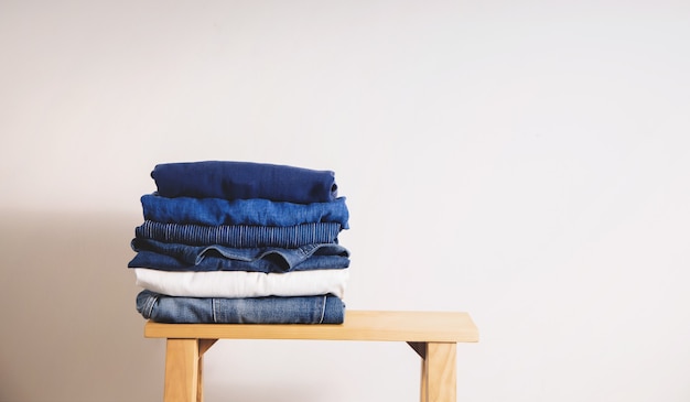 Stack of Clothing on Wooden bench by the White Wall