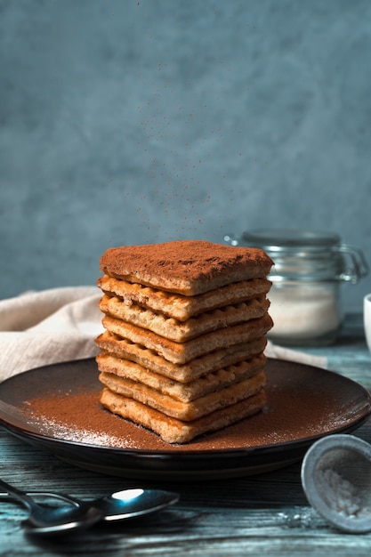 A stack of cocoa-dusted waffles on a wooden gray-blue background.