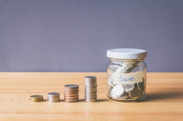 Stack of Coin and Coin in a glass jar on wooden desk, Saving money concept