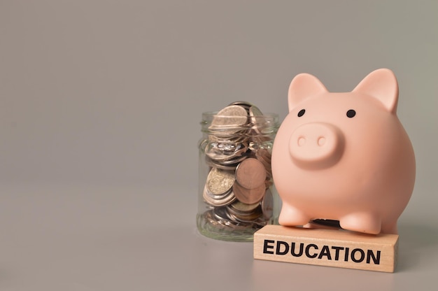 Stack of coins in a glass jar piggy bank and wooden block written with EDUCATION