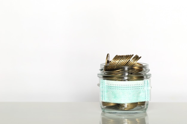 Stack of coins money in glass bottle with wearing protective medical mask on white background, Save money for Medical insurance and Health care concept