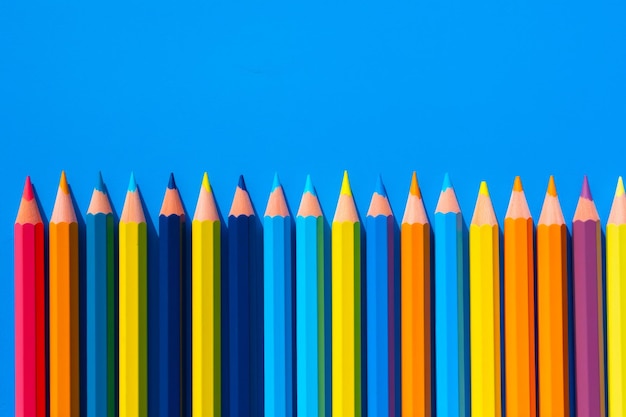 A stack of colored pencils on the blue background wall with copy space