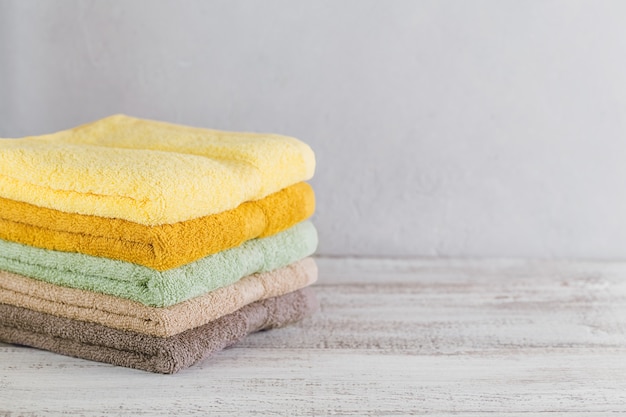 Stack of colorful bath towels on light background. Pastel colors cotton towels. Hygiene, fabric, spa and textile concept