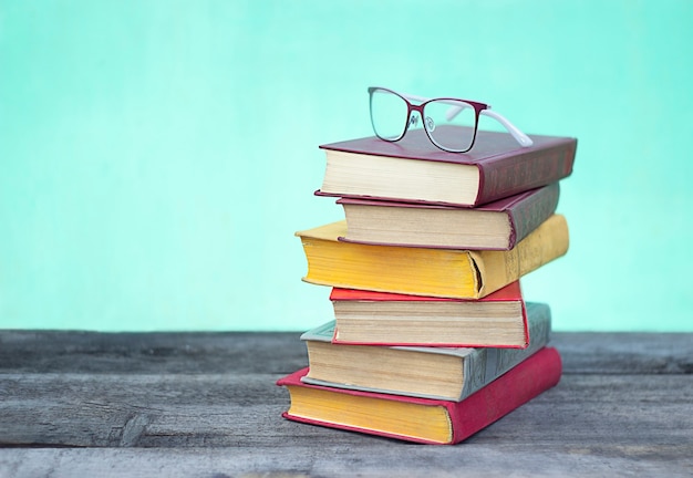 stack of colorful books and glasses on green and blue background