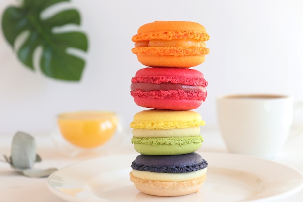 Stack of colorful macaroons on the table with cups of orange juice and coffrr French dessert