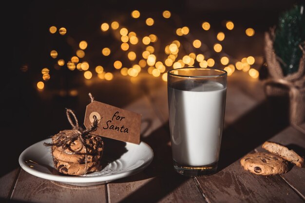 A stack of cookies and glass of milk for Santa on wooden background