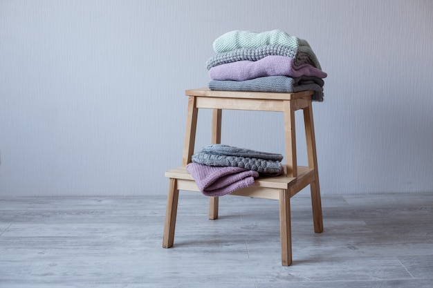 Stack of cozy knitted clothes on a wooden ladder.