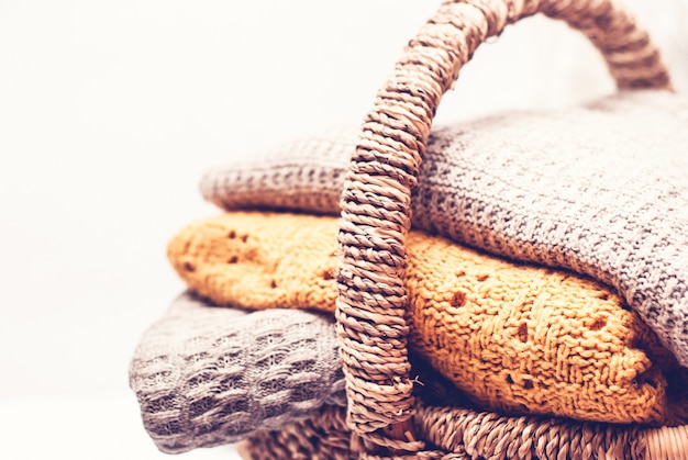 Stack of cozy knitted sweaters in wicker basket