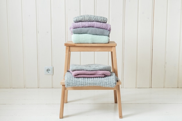Stack of cozy knitted sweaters on a wooden ladder
