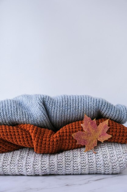 Stack of cozy knitted warm sweater with Autumn fall maple leaf Sweaters in retro Style Orange and blue colors Cozy hygge concept Copy space