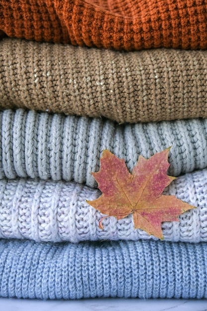 Stack of cozy knitted warm sweater with Autumn fall maple leaf Sweaters in retro Style Orange and blue colors Cozy hygge concept Copy space