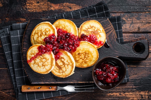 Stack of cranberry syrup pancakes on wooden board. Dark wooden background. Top View.