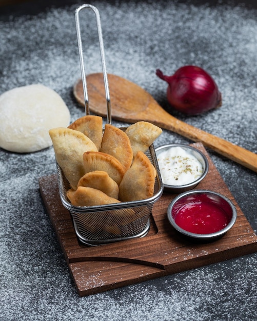 A stack of crispy empanadas with a red onion on a wooden tray.