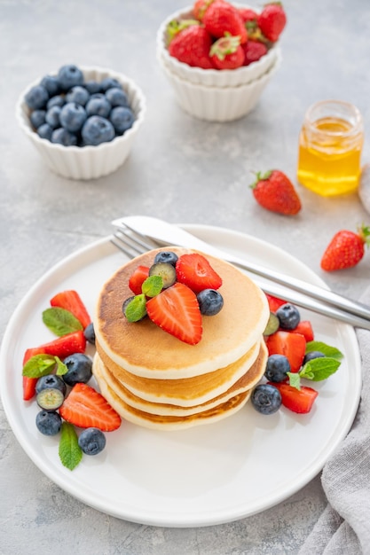 A stack of delicious fluffy pancakes with berries and honey on a white plate Copy space