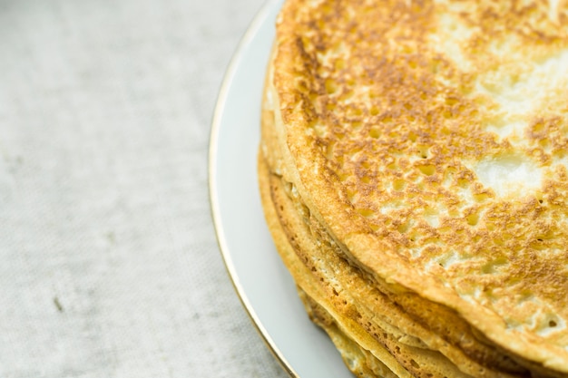 Stack of delicious golden crepes on white plate, on linen cloth background, top view, breakfast