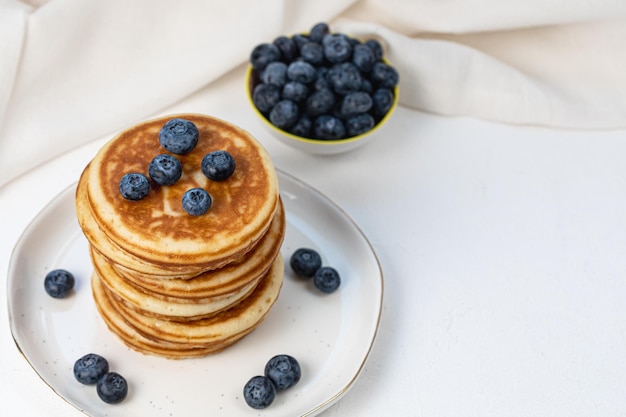 Stack of delicious pancakes on white plate with fresh blueberries on and in bowl top view copy space