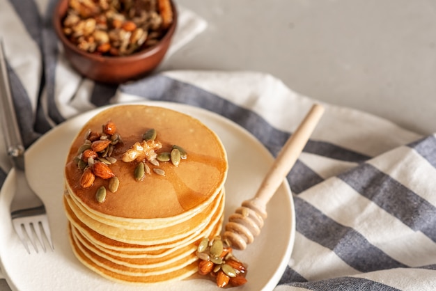 Stack of delicious pancakes with chocolate, honey, nuts and slices of banana on plate and napkin on wooden