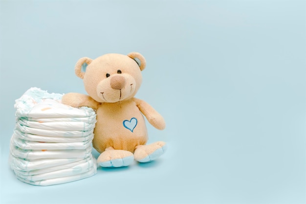 Stack of diapers with cute teddy bear toy on table set for infant newborn boy girl for baby shower present gift on blue background with copy space Healthcare medical hygiene concept