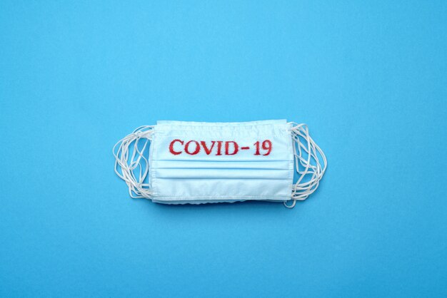 Stack of Disposable blue medical face masks with COVID-19 sign on blue background