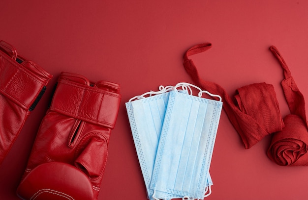 Stack of disposable medical masks, a pair of leather boxing gloves and a red textile bandage