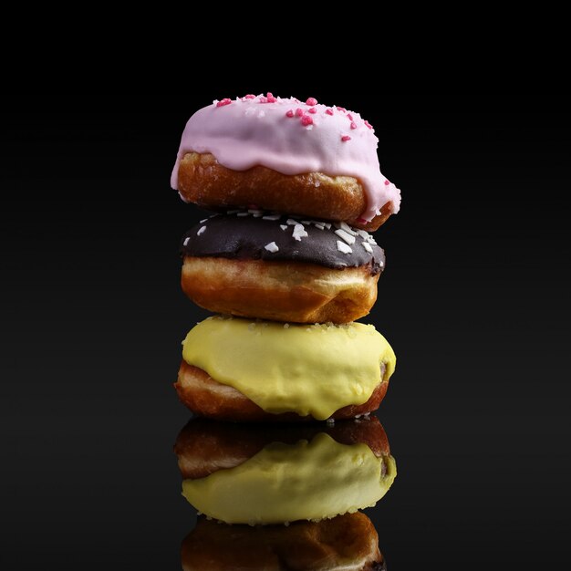 A stack of donuts with icing and chocolate powder, reflected in the mirror. On a black background, isolate, copy space.