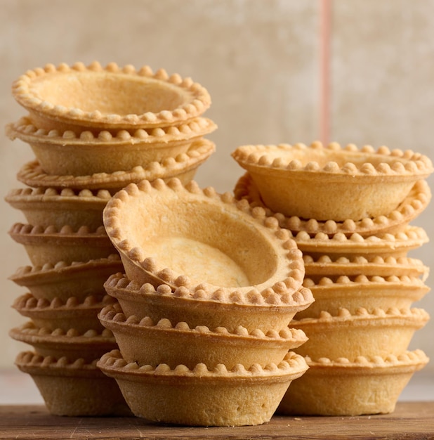 Stack of empty baked round canape baskets on a wooden board round empty tartlets