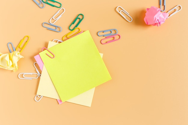 Stack empty sticky post note paper sheet with paper clip on orange background. office business equipment.