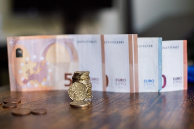 A stack of euro coins stands against the background of paper banknotes of different denominations