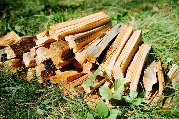 A stack of firewood lying on the green grass on a sunny day outdoors Chopped firewood for the fire