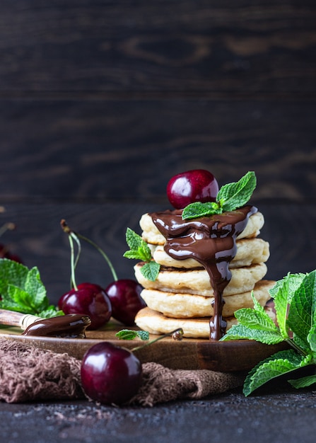 Stack of fluffy pancakes or fritters with chocolate and cherry jam, fresh cherry and mint. 